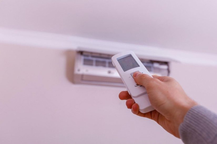 Hand using a remote to control a ceiling-mounted integrated heating and cooling unit in a UAE home